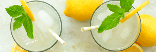 two glasses of lemonade with green mint leaves and a few whole lemons surrounding