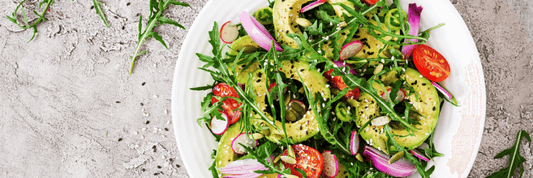 Salad with avocado, red tomatoes, and arugula in white bowl
