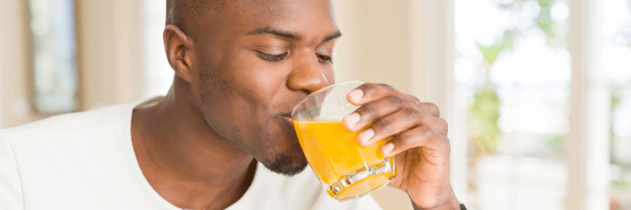Man drinking soursop living bitters with orange juice out of clear glass