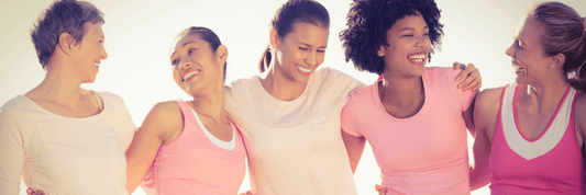 Five women smiling and laughing with each other, wearing pick and white shirts