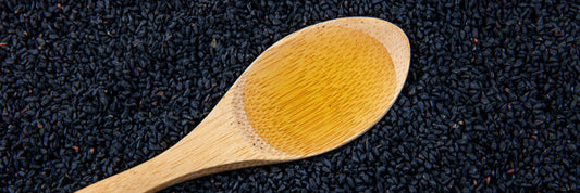 Spoon of Nigella sativa oil over black cumin seeds
