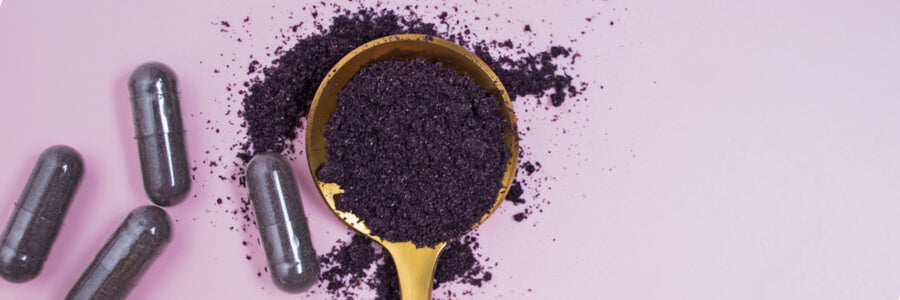 Four purple sea moss capsules next to wooden spoon of purple sea moss powder