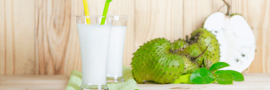 two white soursop drinks next to several green spikey graviola fruit